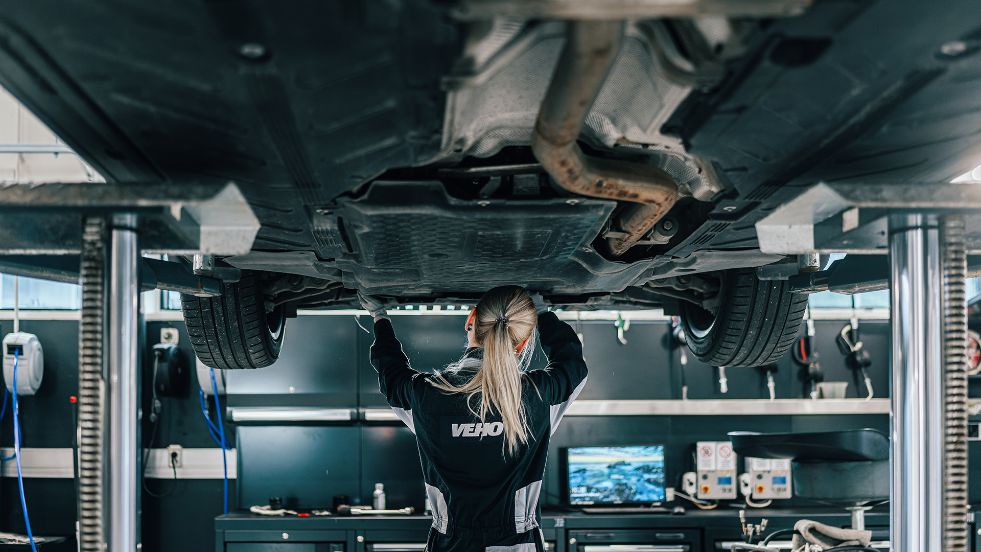 Auto nosturilla, Mercedes-mekaanikko huoltamassa auton alla.